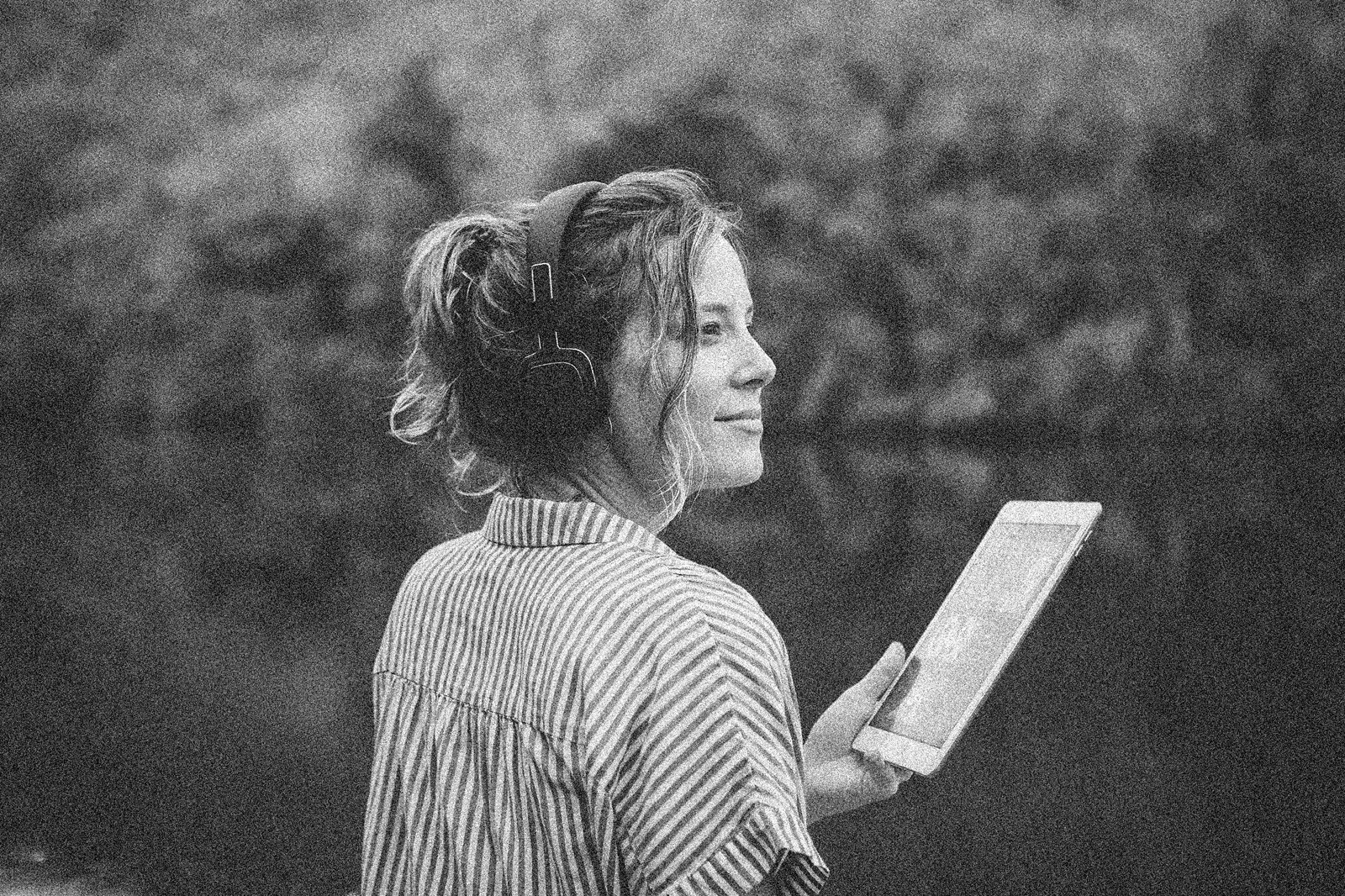 Woman working outdoors with headphones and a tablet