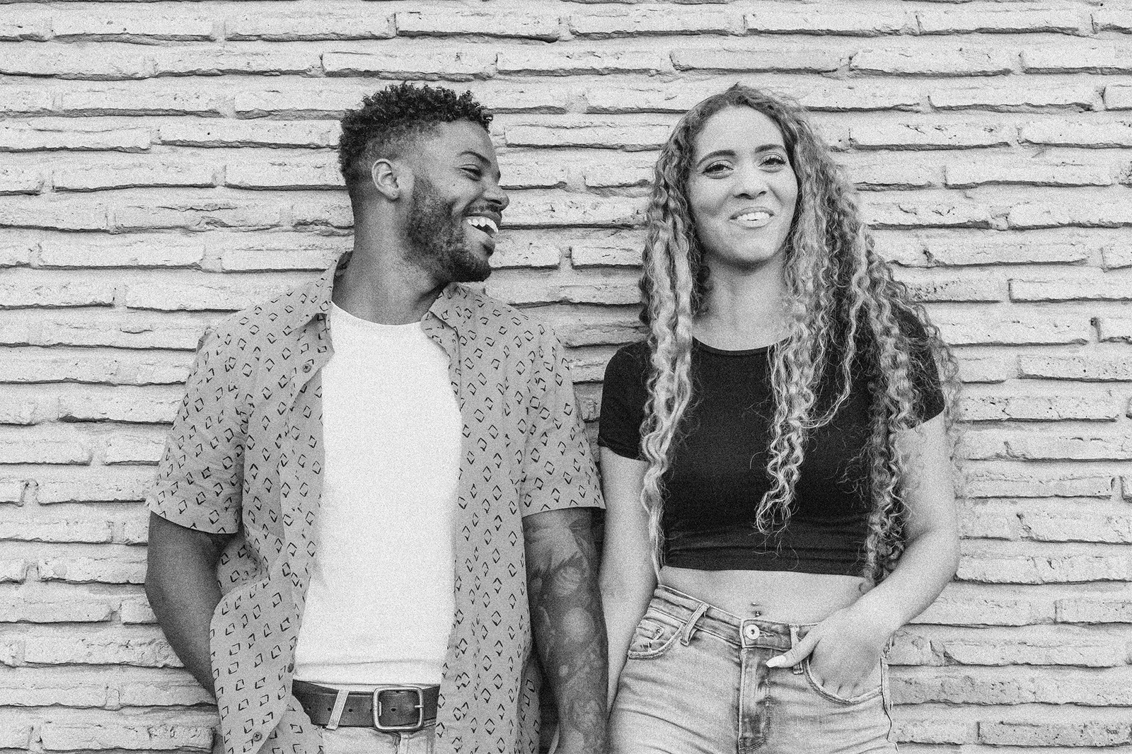 Two friends laughing together against a brick wall